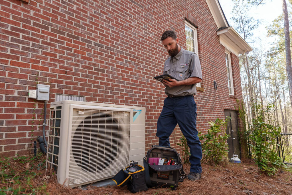 a-technician-reviewing-a-tablet-while-performing-maintenance-on-an-air-conditioning-unit-outside-of-a-customers-home
